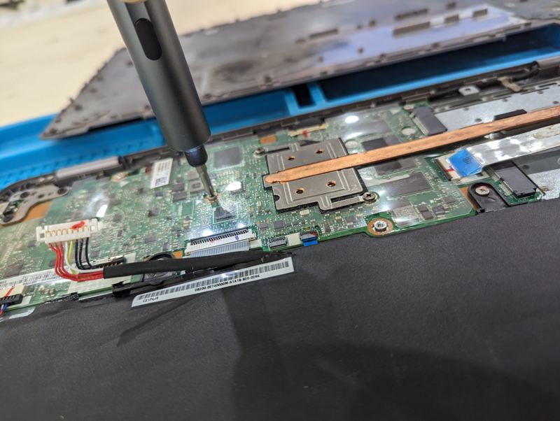 Un tournevis de précision sur la carte mère d'un ordinateur portable ouvert, posé sur un tapis d'atelier bleu.